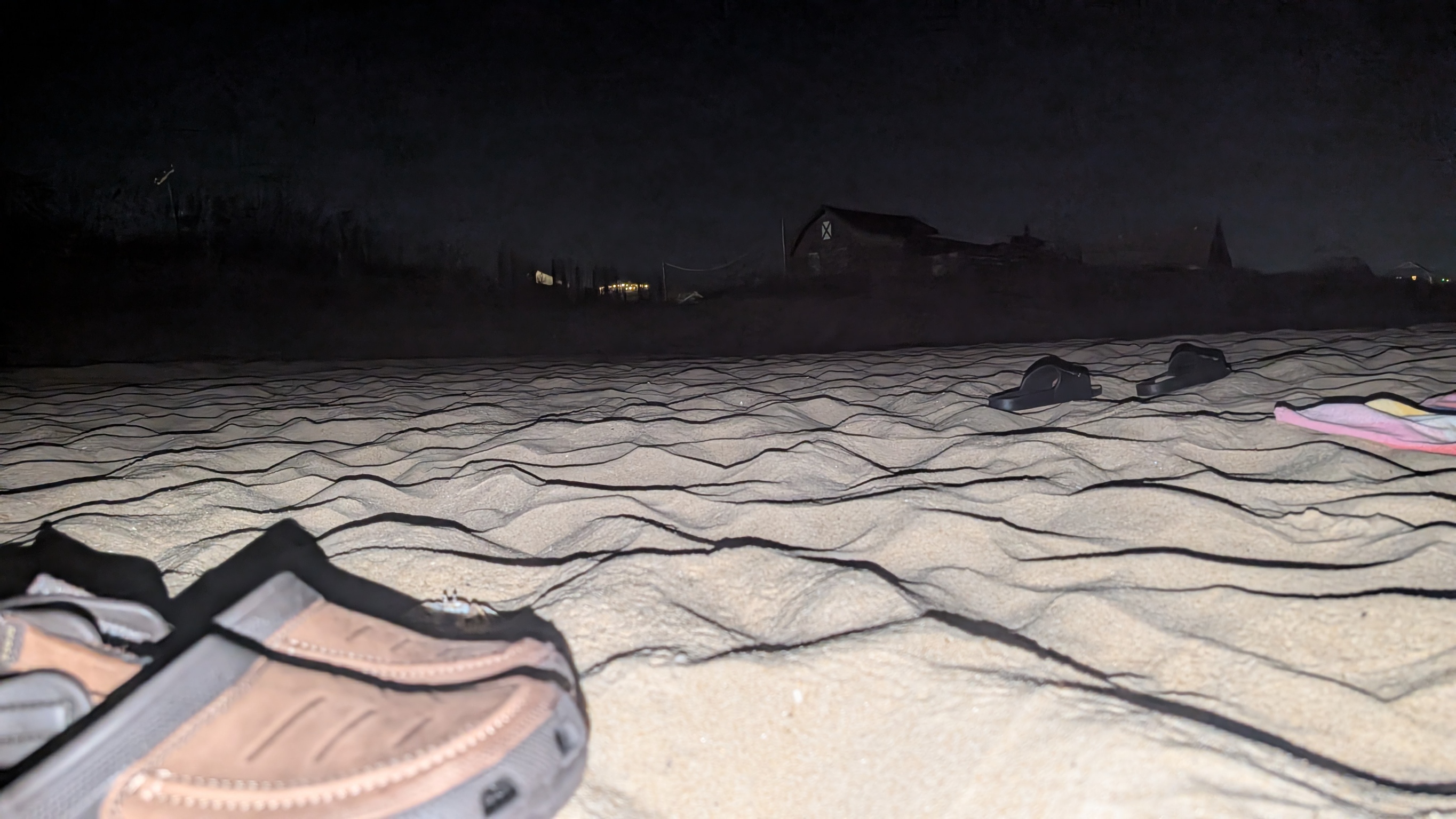Sand and sandals on a beach at night, with buildings in the distance.
